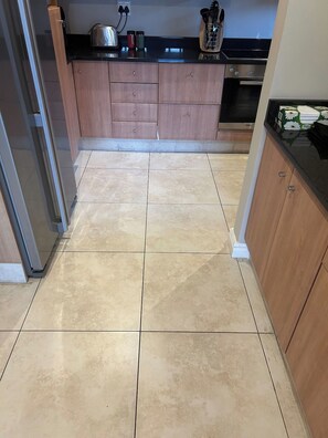 A kitchen with wooden cabinets, a black countertop, and a tiled floor.