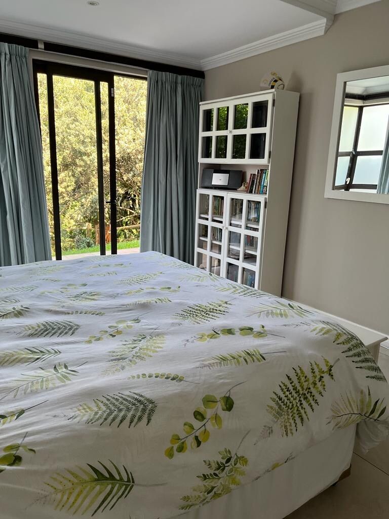Une chambre avec un grand lit, une fenêtre avec des rideaux, une armoire blanche et une vue sur la verdure.