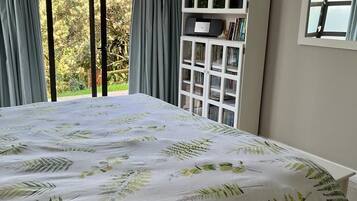 Une chambre avec un grand lit, une fenêtre avec des rideaux, une armoire blanche et une vue sur la verdure.