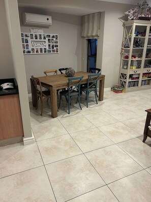 A dining area with a wooden table and chairs, a wall-mounted air conditioner, and a photo collage.