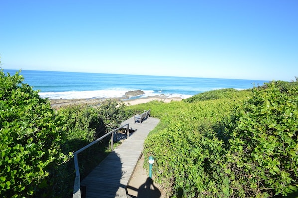 A wooden boardwalk leading to a beach with a clear view of the ocean.