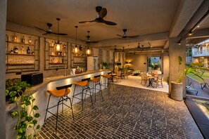 Zona de bar moderna con taburetes altos, ventiladores de techo y suelo con diseño de ladrillo.