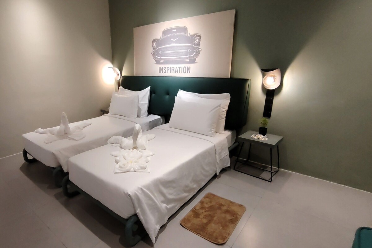 A hotel room with two beds, a headboard, bedside lamps, a small rug, and a wall-mounted artwork.