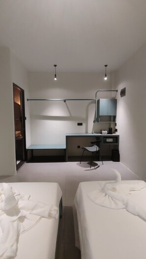 Habitación de hotel con dos camas, un escritorio con silla, una mesita, un espejo y una lámpara colgante.