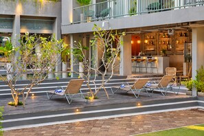 Un espacio al aire libre con sillones de descanso y una barra visible al fondo.