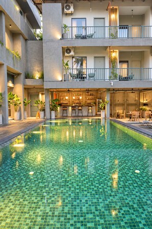 A multi-level hotel with a central swimming pool, outdoor seating, and a bar area. - Grids by Epic Collection (Talpe)