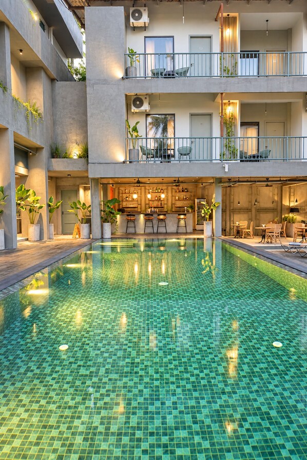 Un hotel de varios niveles con piscina central, mobiliario exterior y zona de bar.