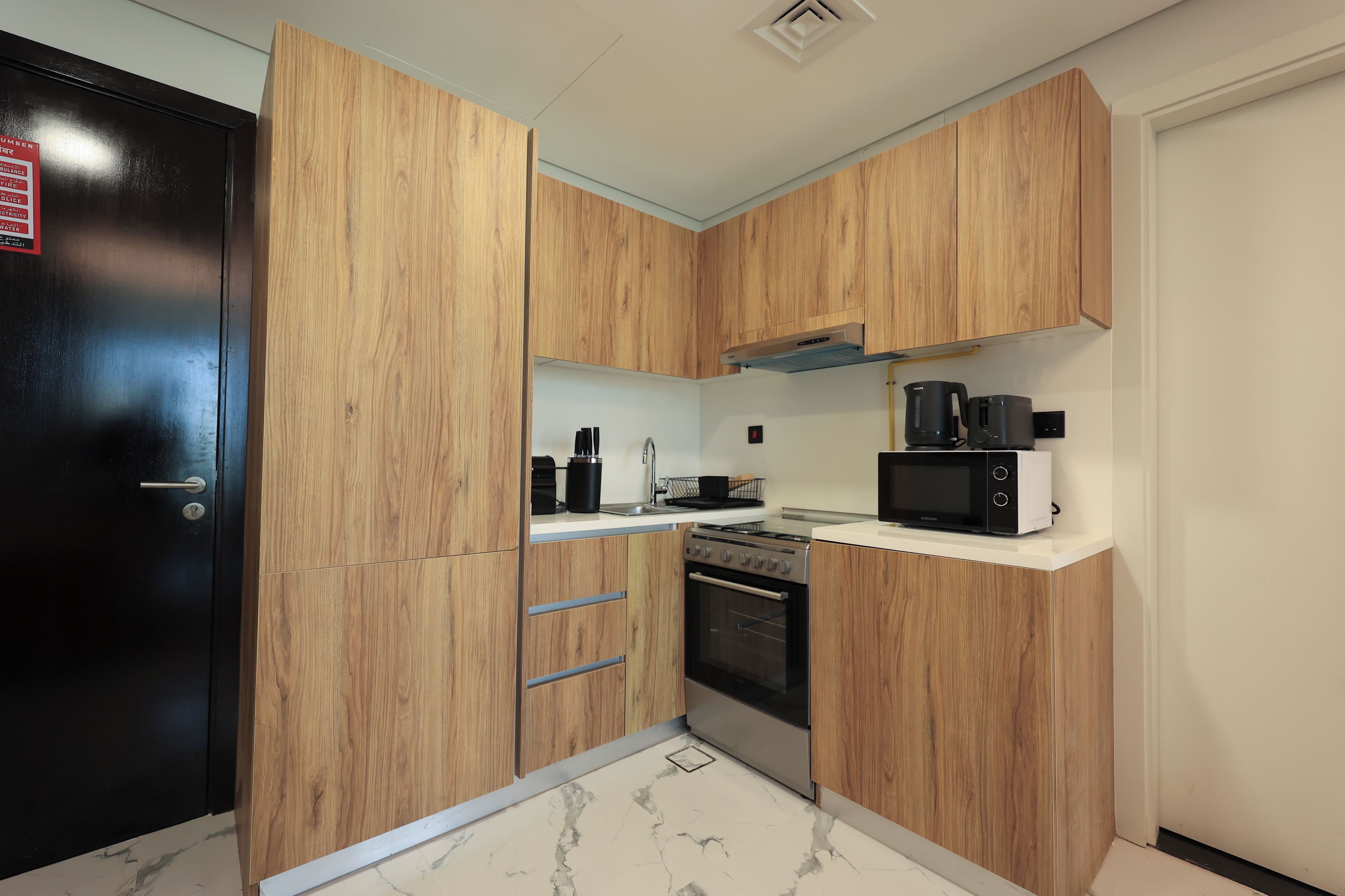 A compact kitchen with wooden cabinets, a black refrigerator, a built-in oven, a microwave, and a coffee maker.