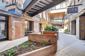 An urban courtyard with a brick wall, a wooden planter with plants, and a sign for a boutique.