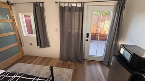 Ein Zimmer mit einem Bett, einem Fernseher, einer Schiebetür mit Vorhängen, einem Fenster und Holzboden.