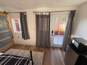 A room with a bed, a TV, a sliding door with curtains, a window, and a wooden floor.