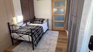 Ein Schlafzimmer mit einem Bett, einem Fenster mit Jalousien, einer Tür und Holzboden.