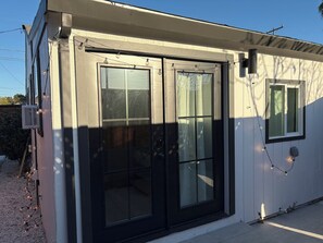 Un petit bâtiment doté d’une fenêtre à cadre noir et d’une porte, d’une petite fenêtre et d’une prise de courant sur le mur.