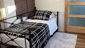 Ein Bett mit einer schwarz-weiß karierten Tagesdecke, einem Holzkopfstück und einer weißen Wand mit einem Fenster.