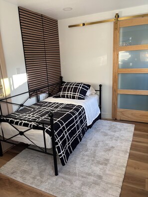 A bed with a black and white checkered bedspread, a wooden headboard, and a white wall with a window.