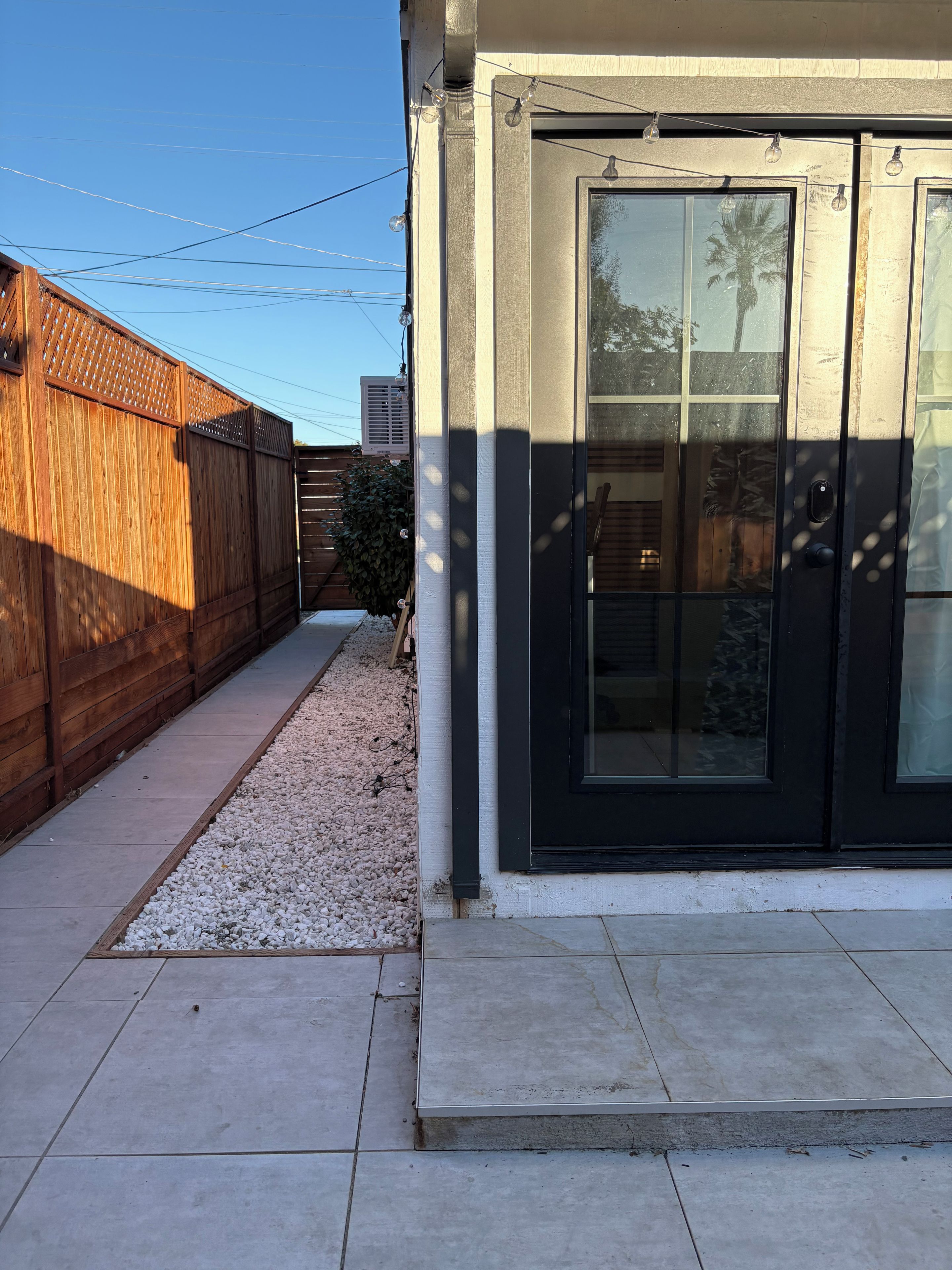 A residential property with a paved patio, a wooden fence, and a black-framed door.