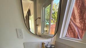 Ein Badezimmer mit einem weißen Waschbecken, einem Spiegel, einem Fenster und einer Toilette.