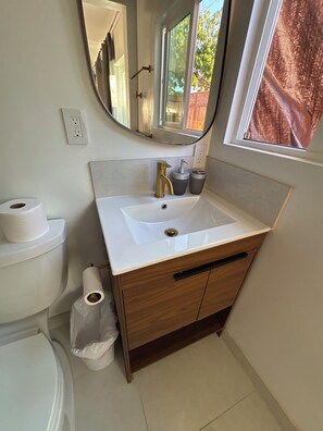 A bathroom with a white sink, a mirror, a window, and a toilet.
