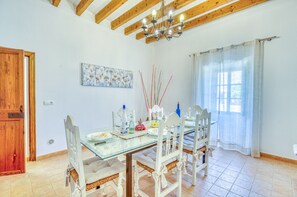 A dining area with a glass table, white chairs, a chandelier, and a window with curtains. - Finca with pool Son Manyo Gran I Sa Pobla (Sa Pobla)