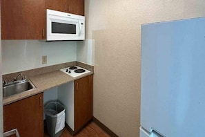 Una cocina compacta con microondas, lavamanos y un cubo de basura.