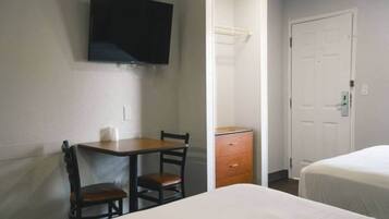 A hotel room with a bed, a desk with two chairs, a television mounted on the wall, and a door.