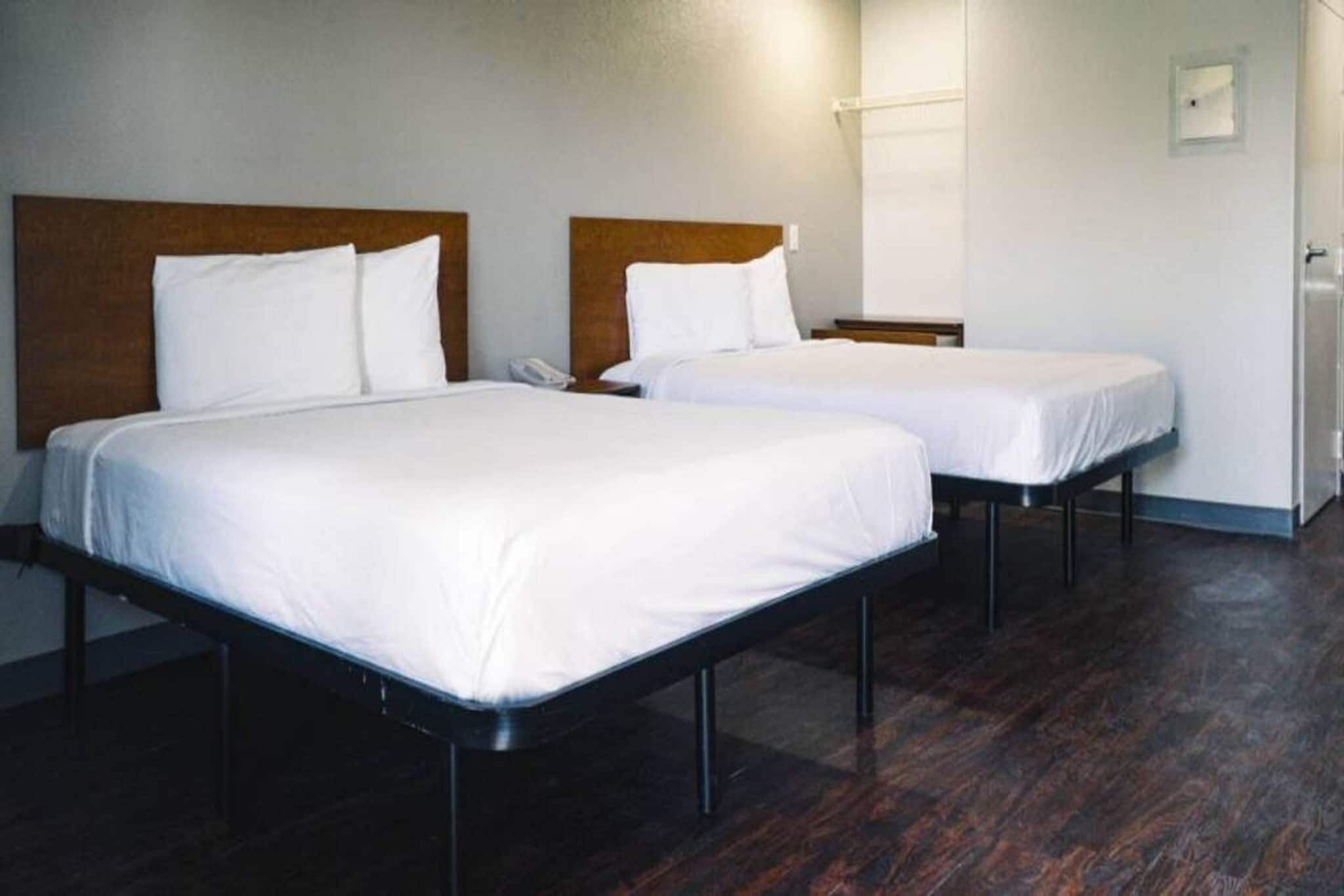 Duas camas de solteiro com cabeceiras de madeira num quarto com soalho de madeira escura e paredes brancas.