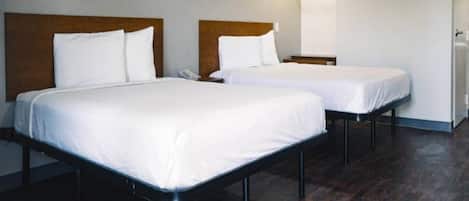 Two single beds with wooden headboards in a room with dark wooden flooring and white walls.