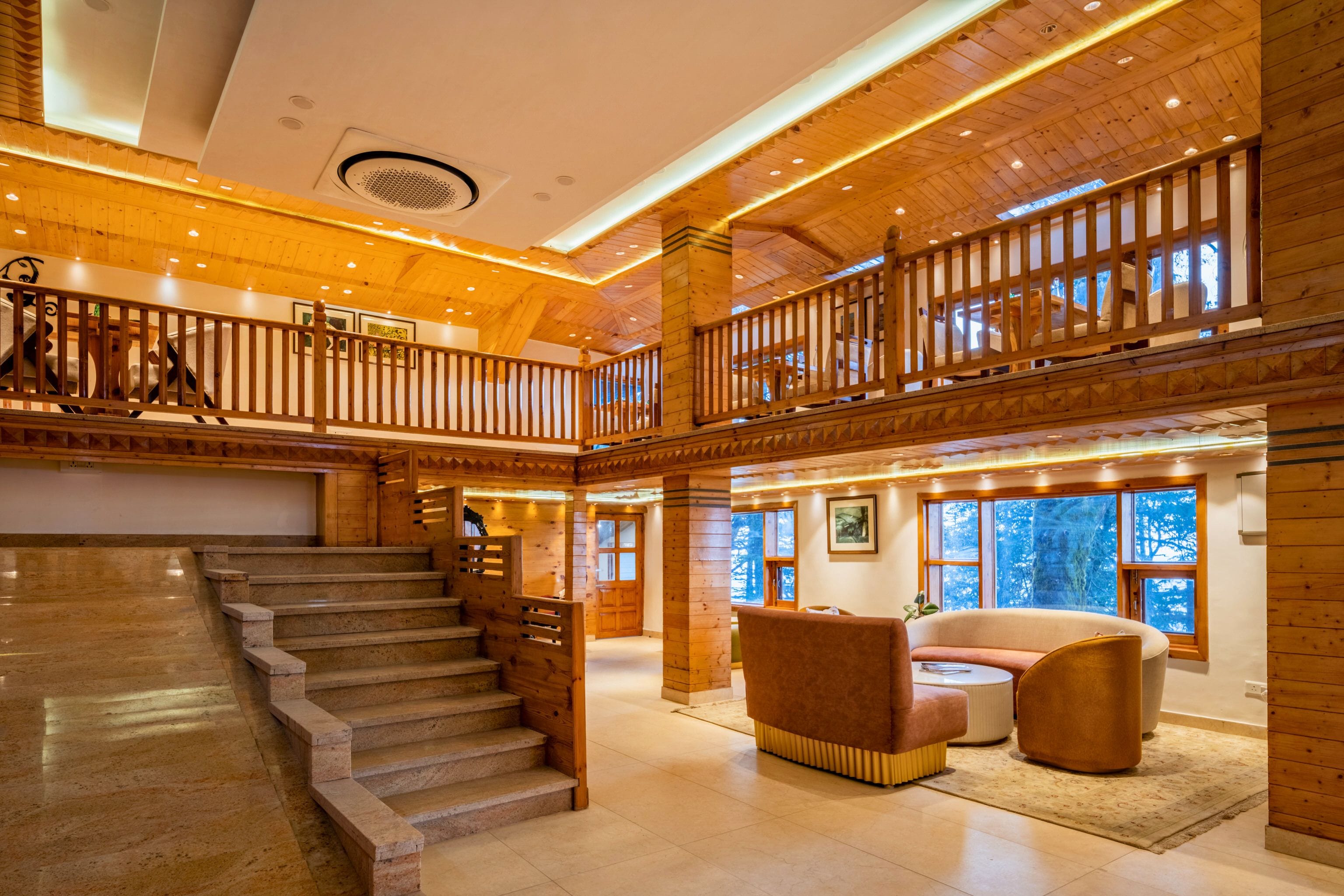 A spacious lobby with a grand staircase, wooden railings, and a seating area with a sofa and armchairs.