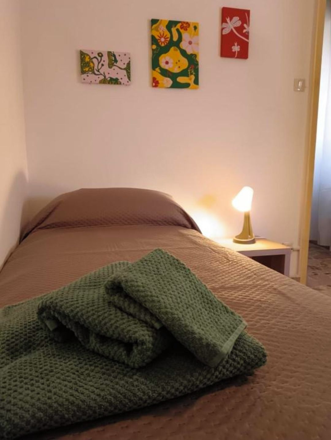 Ein Schlafzimmer mit einem Bett, einer grünen Decke, einem Nachttisch mit Lampe und drei Wandbildern.