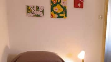 Ein Schlafzimmer mit einem Bett, einer grünen Decke, einem Nachttisch mit Lampe und drei Wandbildern.