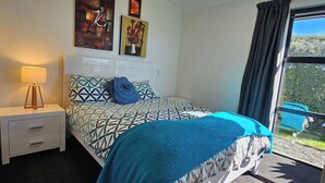 Een slaapkamer met een bed, een nachtkastje met een lamp, en twee schilderijen aan de muur.