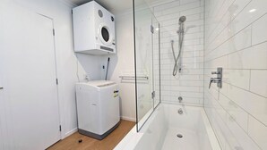 Een moderne badkamer met een douchecabine van glas, een ingebouwde wasmachine en een betegelde muur in het wit.