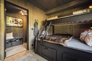 Een gezellige kamer met een stapelbed, een ladder, een klein tafeltje met flessen en een schilderij aan de muur.
