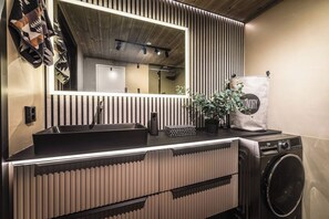 Een moderne badkamer met een zwarte wastafel, een spiegel, een wasmachine en een potplant.