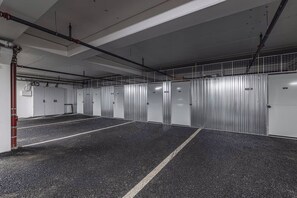Een parkeergarage met meerdere rijen parkeerplaatsen, metalen inbouwkasten en zichtbare leidingen aan het plafond.