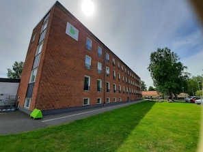 A multi-story brick building with a flat roof, a green lawn in front, and a clear sky.