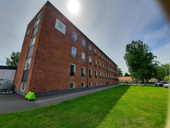 Un edificio de varios pisos de ladrillo con techo plano, un césped verde en la parte delantera y un cielo despejado.