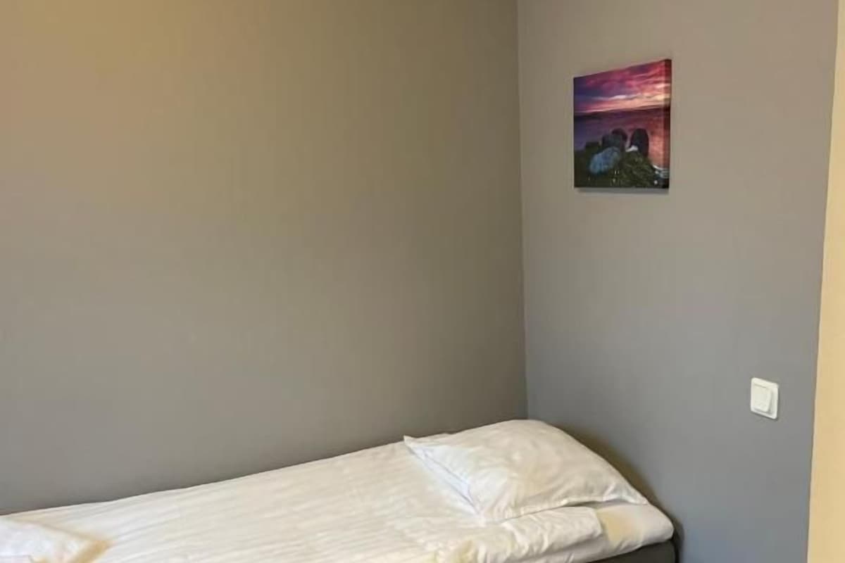 Una cama individual con colchón acolchado y almohadas, una mesita de noche de madera y un cuadro colgado en la pared.