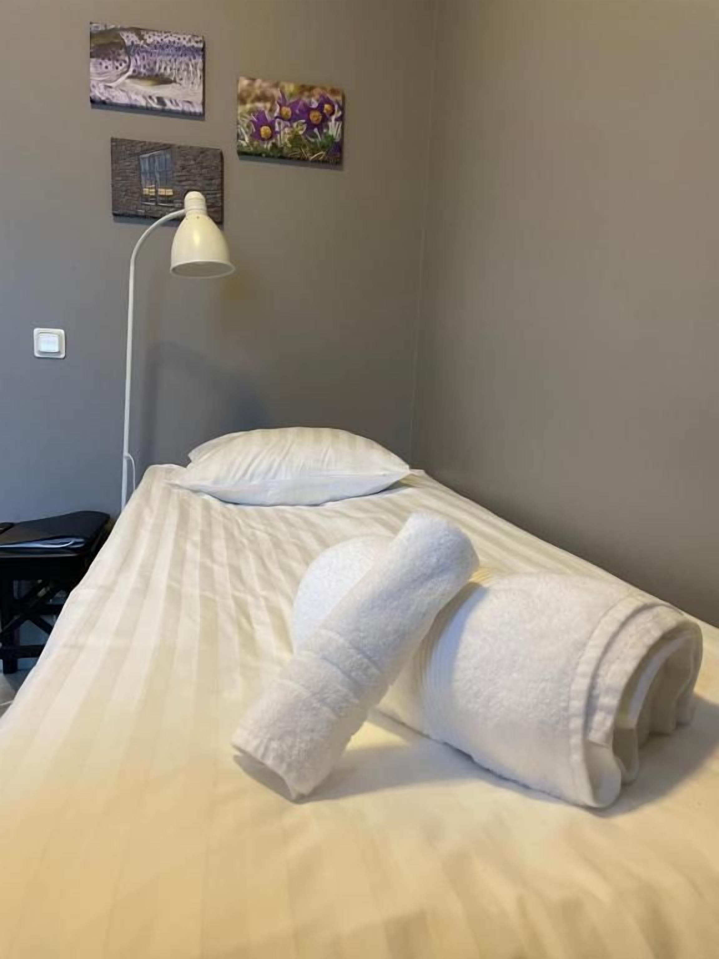 Cama bem arrumada com toalha branca enrolada, abajur e obra de arte na parede.