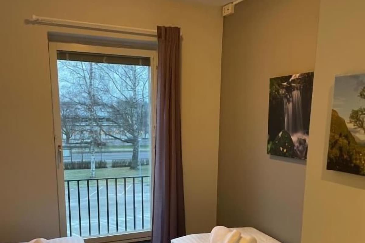 Una habitación de hotel con dos camas, un ventanal con vistas a un parque y un cuadro en la pared.