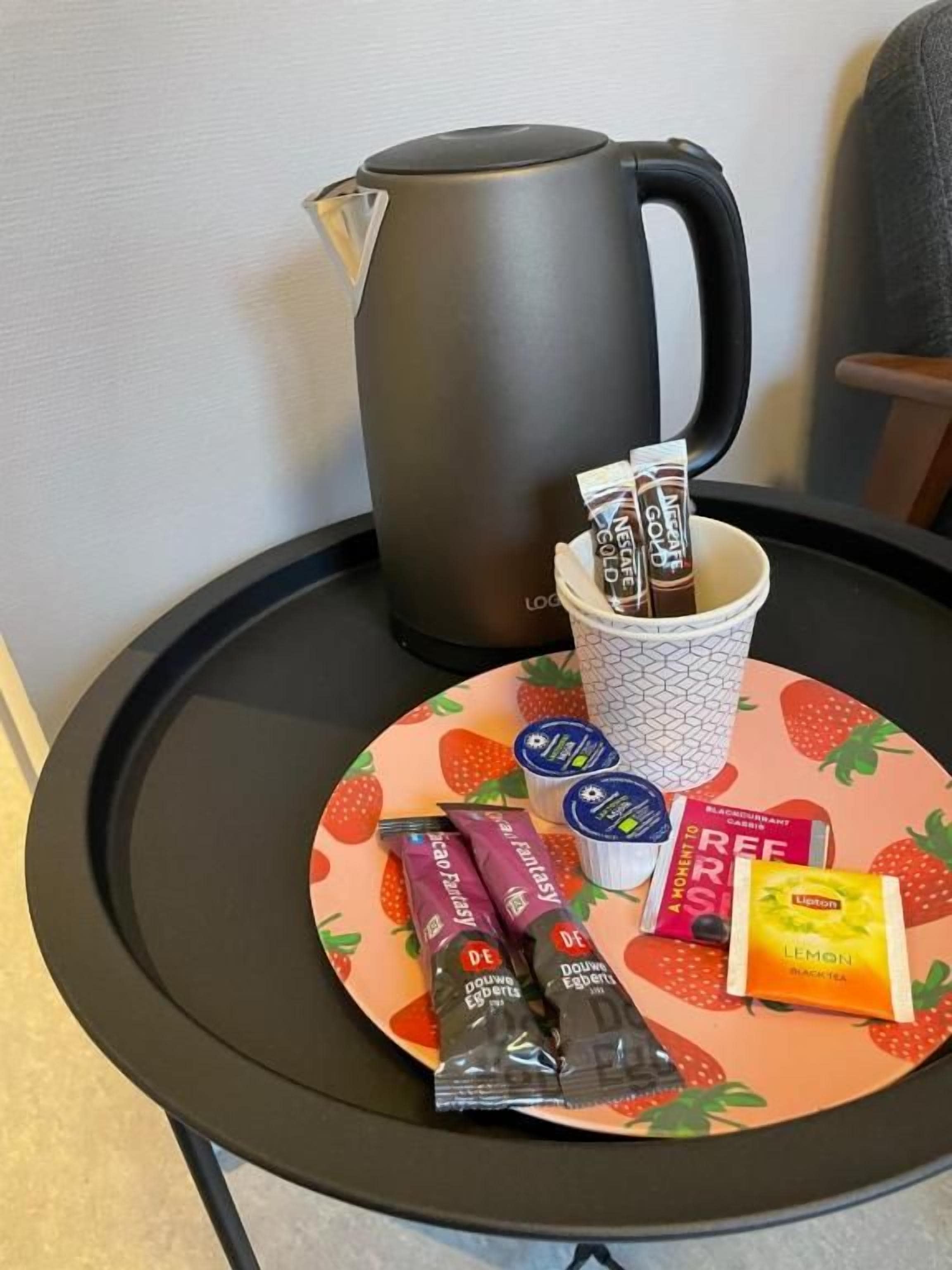 A table with a coffee pot, a cup of coffee, and various food items including chocolate and lemon tea packets.