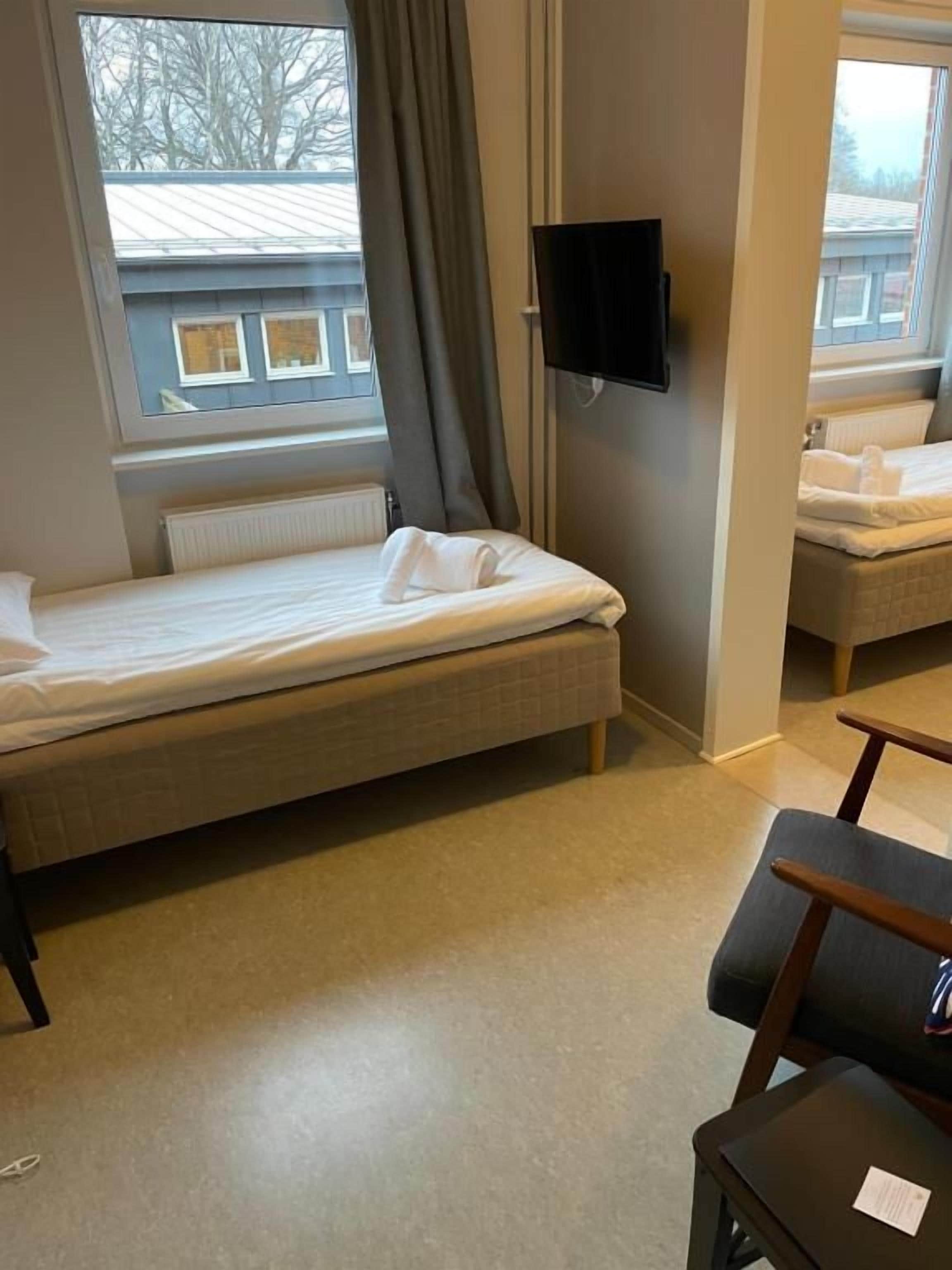 A hotel room with a bed, a chair, a table, a TV, and a window with curtains.