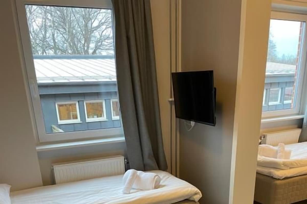 Habitación de hotel con cama, una silla, una mesa, un televisor y una ventana con cortinas.