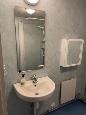 Un baño con un lavamanos blanco, un espejo, cabina de ducha y un armario blanco.