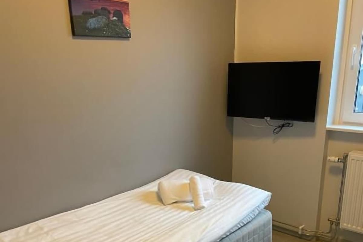 Una cama individual con colchón acolchado, un televisor de pantalla plana en la pared y un radiador.