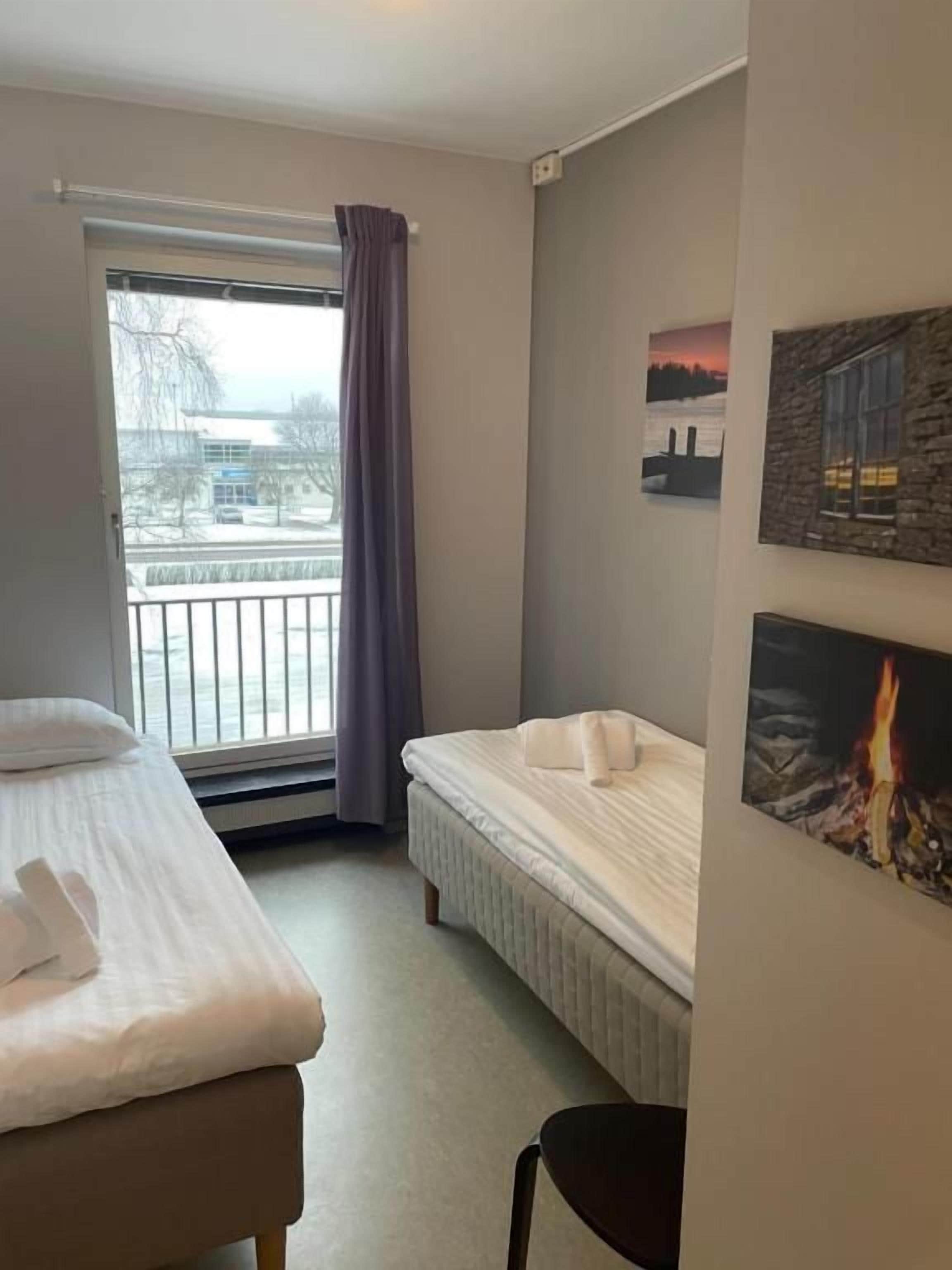 Una habitación de hotel con una cama, una silla, una ventana que ofrece vistas al exterior y una pared con un cuadro.