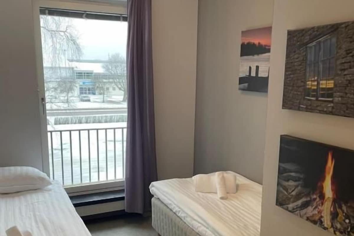 Una habitación de hotel con una cama, una silla, una ventana que ofrece vistas al exterior y una pared con un cuadro.