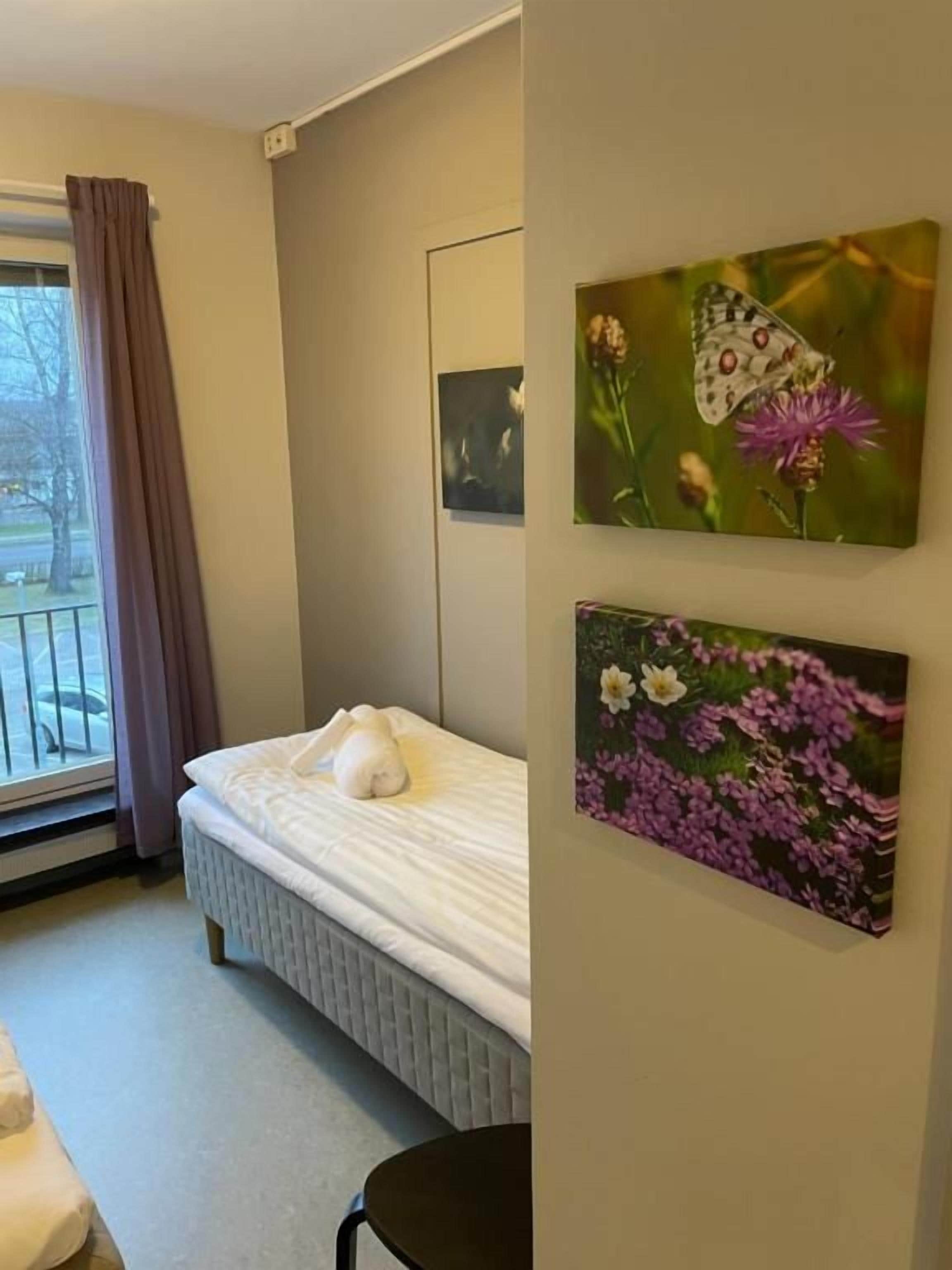 A bedroom with a bed, a window with curtains, and two wall-mounted paintings.