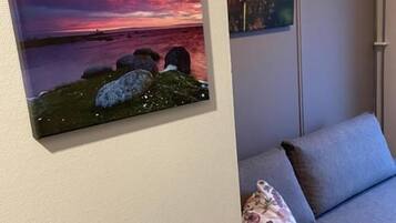 A room with a grey sofa, a painting of a sunset, and a smaller artwork on the wall.
