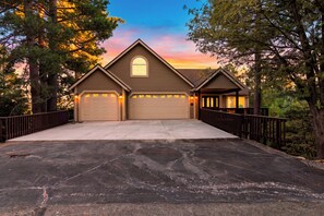 Un garage accolé à une maison, pouvant accueillir deux voitures, avec un porche abrité et entouré d’arbres.